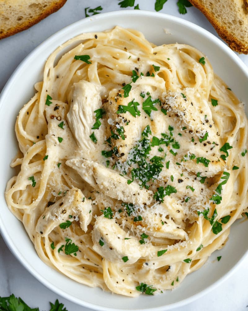 Bowl of fettuccine in creamy Alfredo sauce topped with sliced chicken, grated parmesan, black pepper and chopped parsley