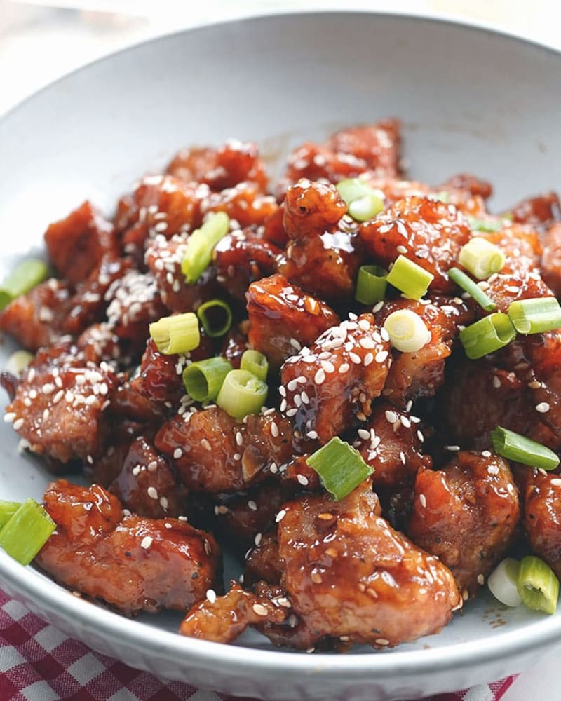 Glazed chicken teriyaki pieces topped with sesame seeds and sliced scallions in a gray bowl